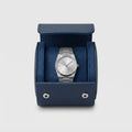 Étui vu de face, ouvert, montre bracelet acier posée dans le berceau en suédine bleu marine.
