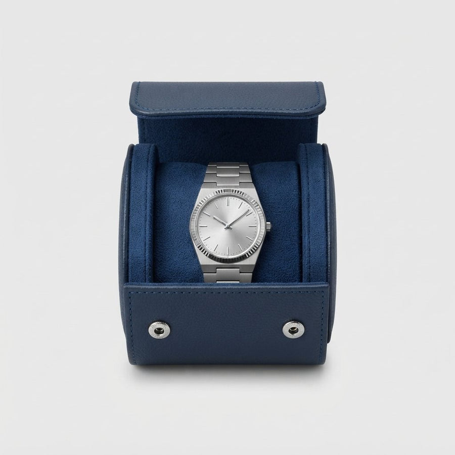 Étui vu de face, ouvert, montre bracelet acier posée dans le berceau en suédine bleu marine.