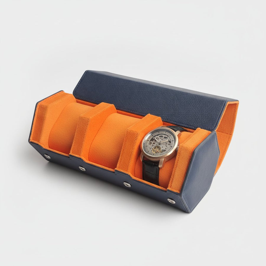 Étui ouvert, montre à cadran squelette logée dans l'un des trois compartiments, extérieur bleu marine et doublure orange.