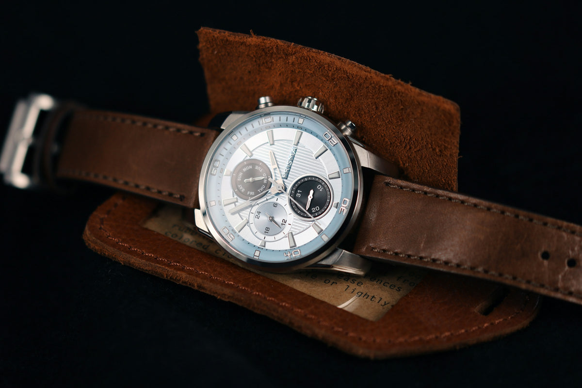 Une montre chronographe glissée dans un étui en cuir, sur fond noir