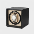 Cube noir mat, coussin crème, montre en place, vue de trois quarts, fond clair.