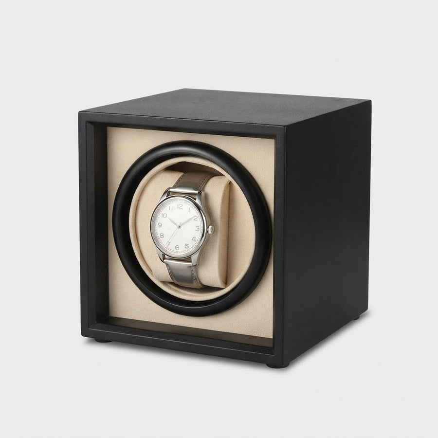 Cube noir mat, coussin crème, montre en place, vue de trois quarts, fond clair.